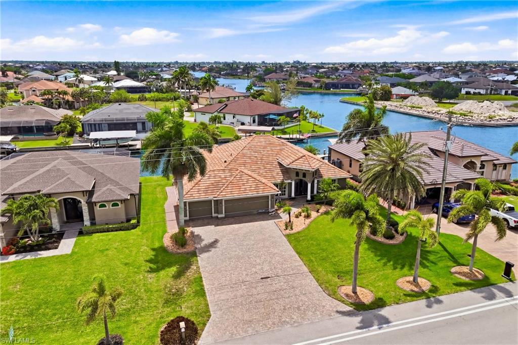 Image 3: Waterfront property featuring mature palm trees, a concrete driveway, and a tile roof