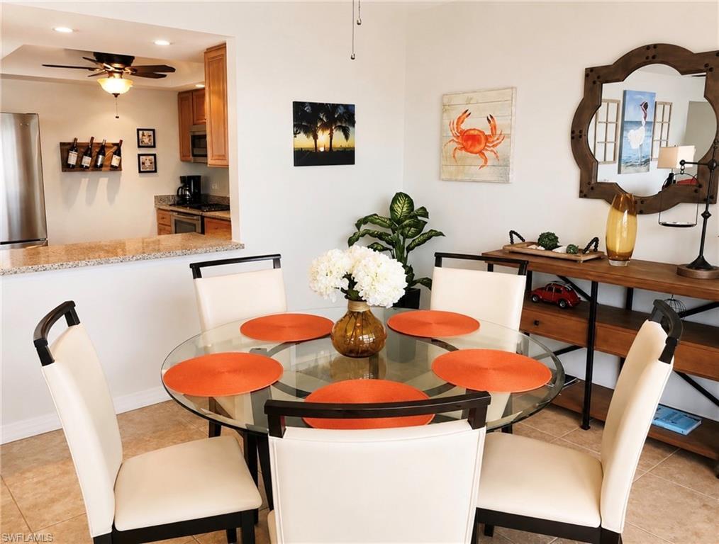Image 2: Open-concept dining area featuring tile flooring, a half wall with a granite countertop, and a pass-through opening to the kitchen with light wood cabinetry and a ceiling fan
