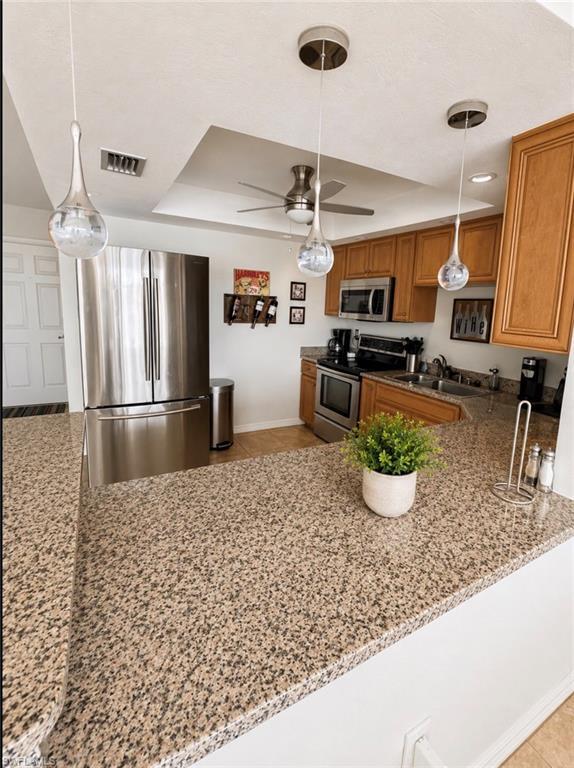 Image 4: Kitchen featuring granite countertops, stainless steel appliances, wood cabinetry, contemporary pendant lighting, and a recessed ceiling with a ceiling fan