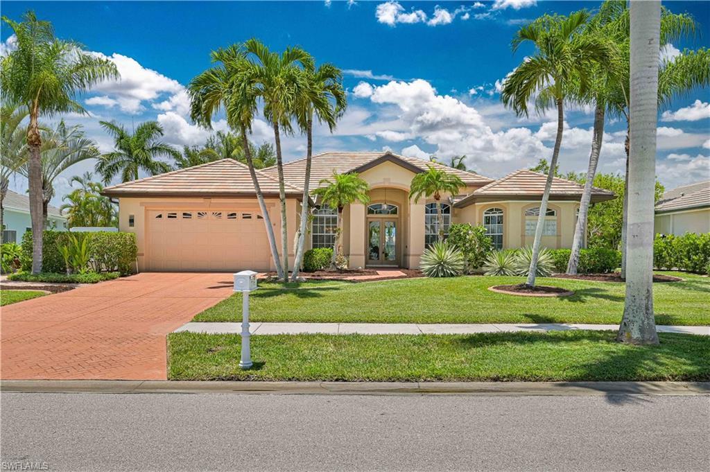 Image 2: Stucco exterior with a tiled roof, featuring a brick paver driveway, an attached garage, and mature palm trees