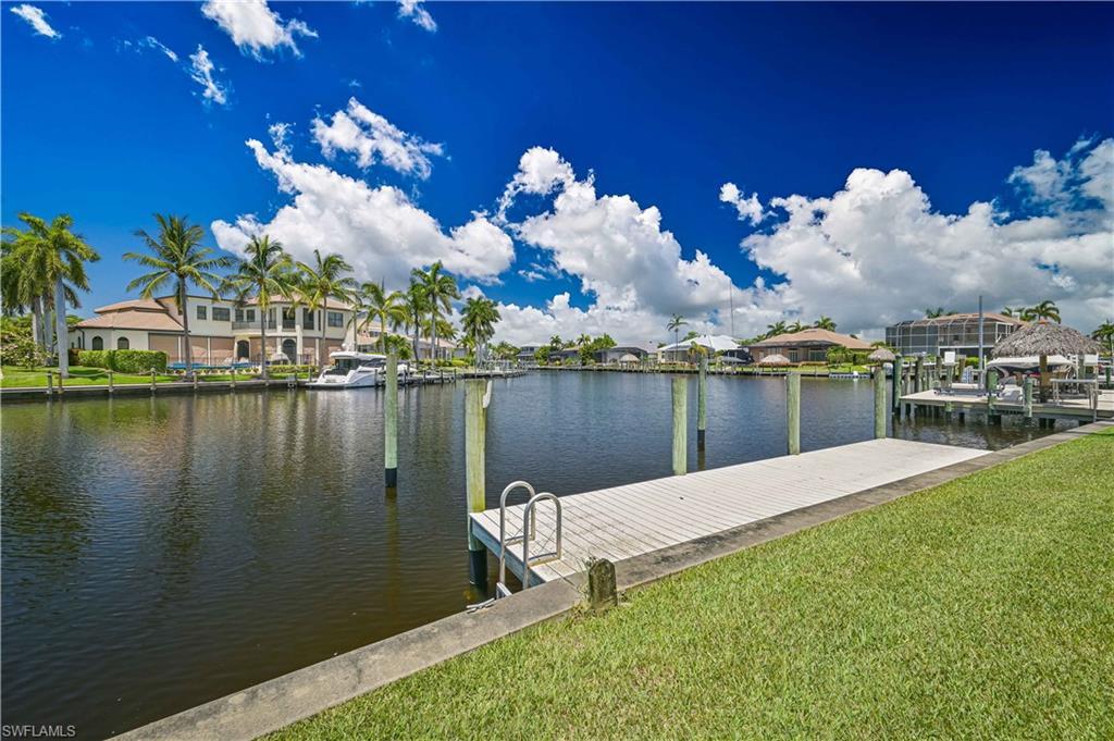 Image 4: Waterfront property featuring a private boat dock with a ladder, lush green lawn, concrete seawall, and mature palm trees