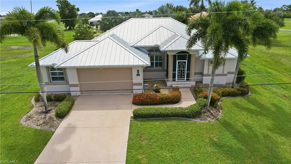 Image 1: Elegant contemporary residence featuring a metal roof with clean geometric lines, two-car garage with paneled door, and mature landscaping including palm trees and manicured foundation plantings