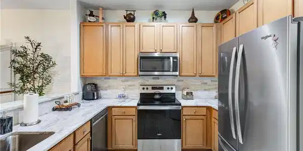 Image 4: Efficient kitchen featuring warm wood cabinetry, stainless steel appliances including a built-in microwave and electric range, white subway tile backsplash, light countertops, tile flooring, and a side-by-side refrigerator with ample storage and workspace