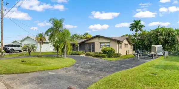 Image 4: Paved driveway with ample parking, mature palm trees, and established landscaping
