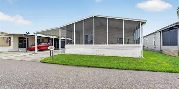 Image 2: Screened porch with privacy screening, attached carport, concrete driveway, and a well-maintained lawn