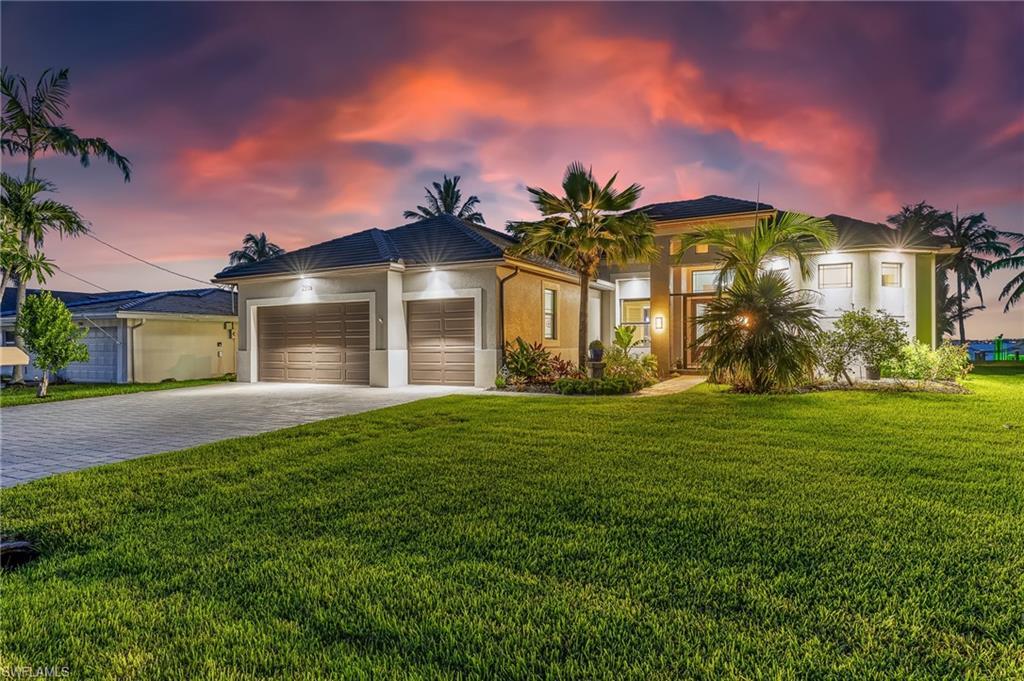 Image 2: View of front of property featuring an attached garage, decorative driveway, a lawn, and stucco siding