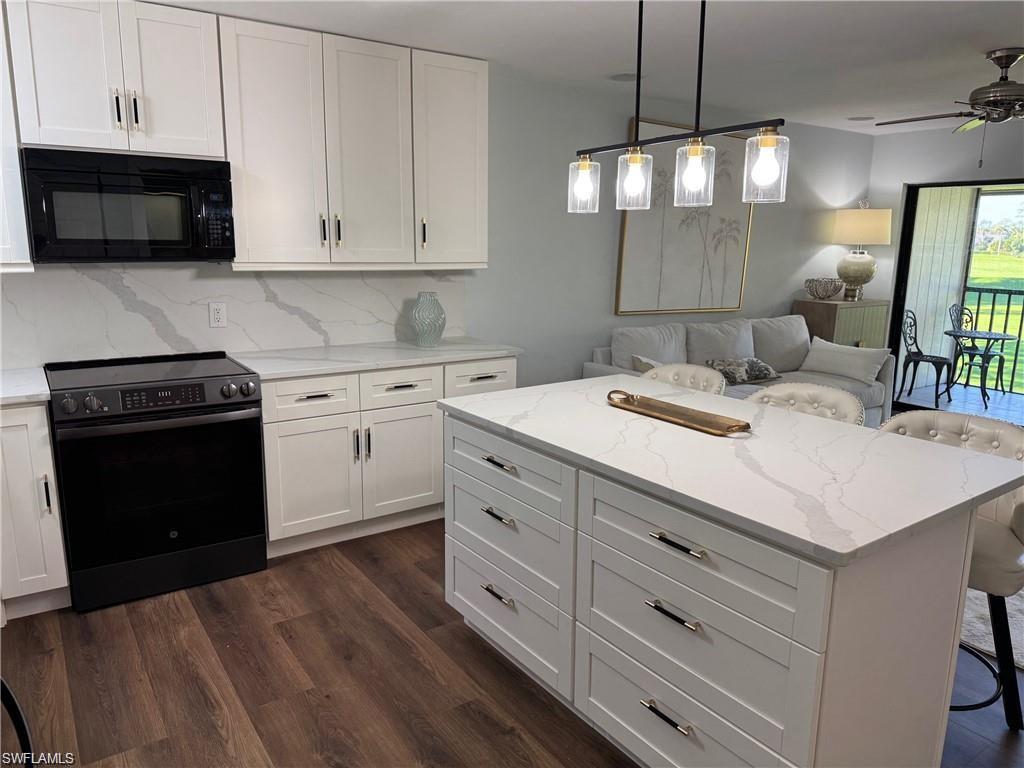 Image 4: Kitchen with electric range, a breakfast bar, black microwave, white cabinets, and open floor plan