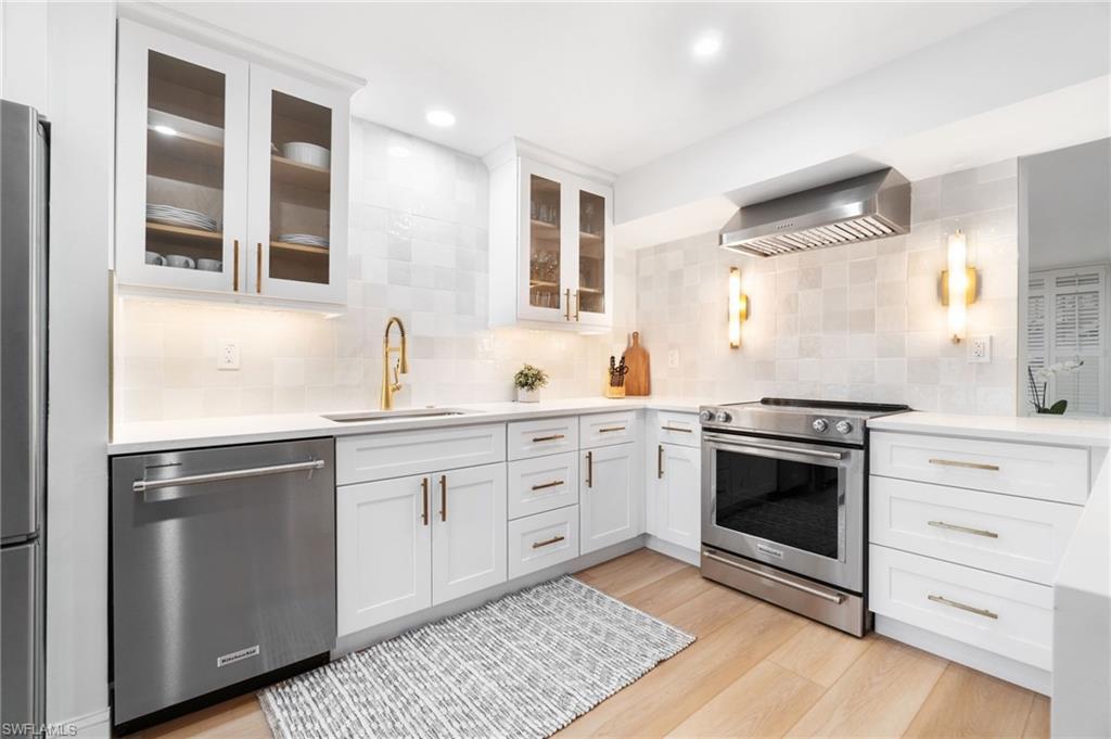 Image 4: Kitchen with stainless steel appliances, white cabinetry, light stone countertops, backsplash, and light wood-style flooring