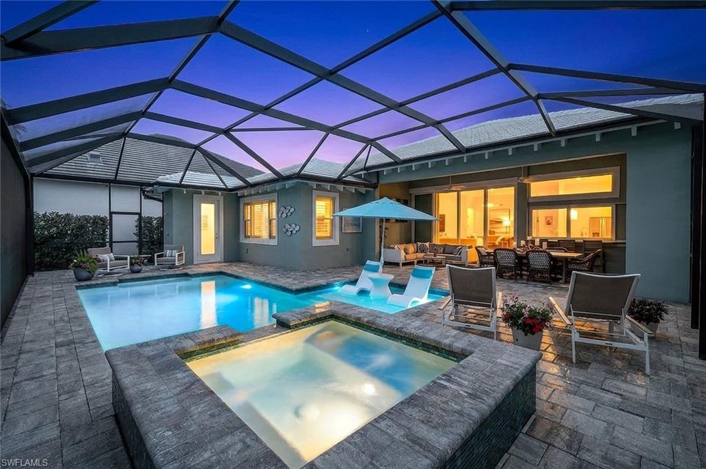 Image 1: Pool at dusk with outdoor furniture, a sunroom, a pool with connected hot tub, and glass enclosure