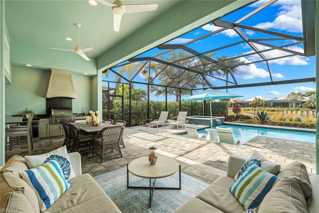 Image 3: View of patio / terrace with exterior kitchen, a sunroom, a pool with connected hot tub, glass enclosure, and an outdoor living / dining area