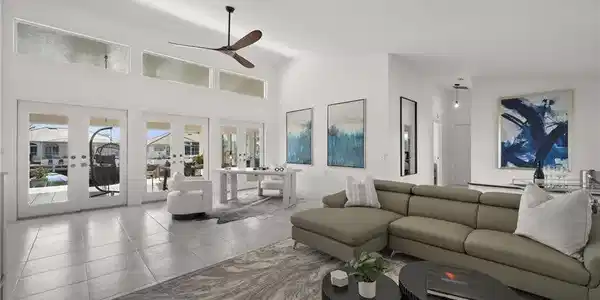 Image 4: The living area features high ceilings, a ceiling fan, and large windows with French doors that provide an abundance of natural light and views of the surrounding properties and waterway