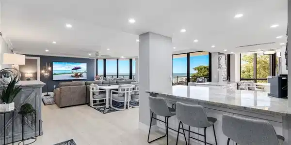 Image 3: This open-concept living space features light-toned flooring, recessed lighting, and expansive windows offering views of the outdoors