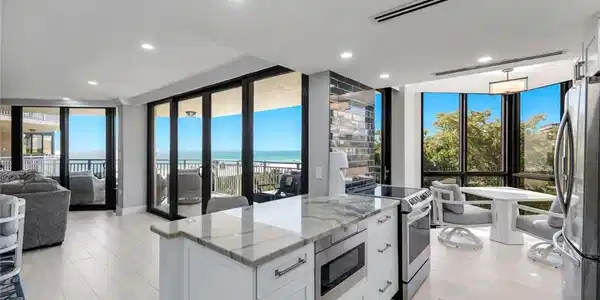 Image 4: Open concept living area featuring light-toned flooring, a kitchen island with a stone countertop, and stainless steel appliances