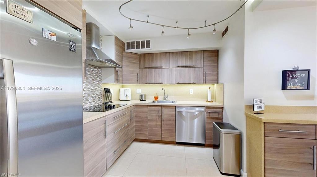 Image 2: Kitchen featuring wood-finish cabinetry, stainless steel appliances, a tiled backsplash, and recessed under-cabinet lighting