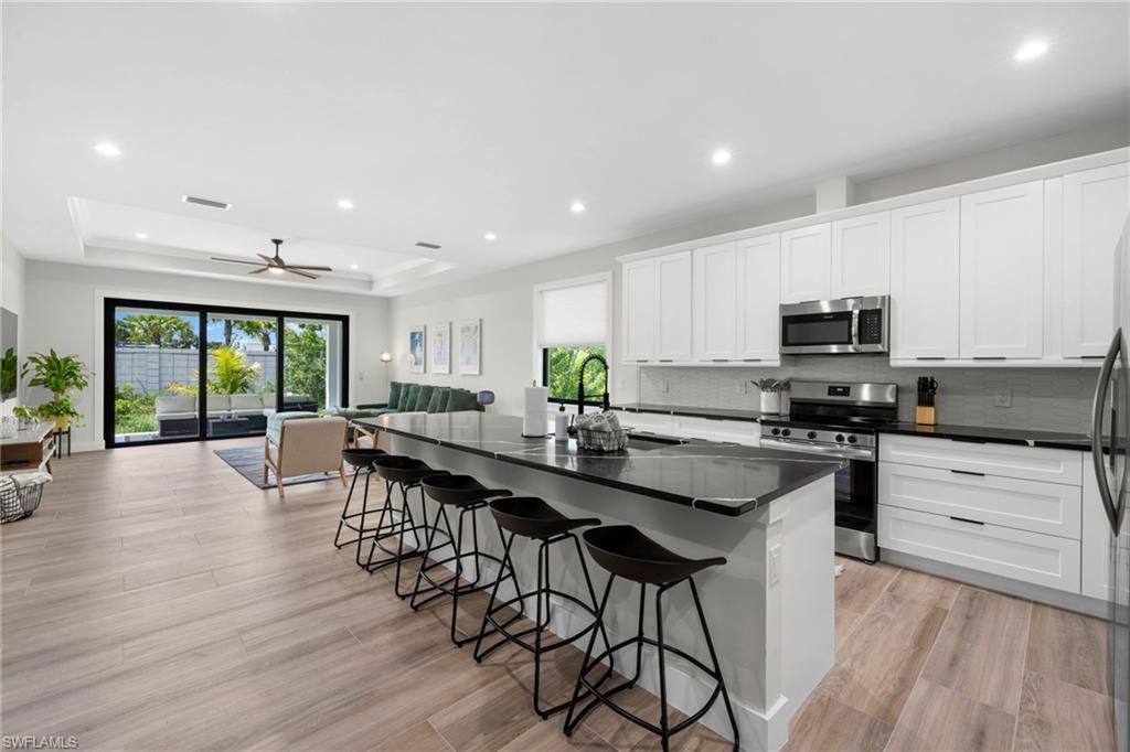 Image 3: Contemporary kitchen featuring white cabinetry, stainless steel appliances, dark countertops, and a large island with seating