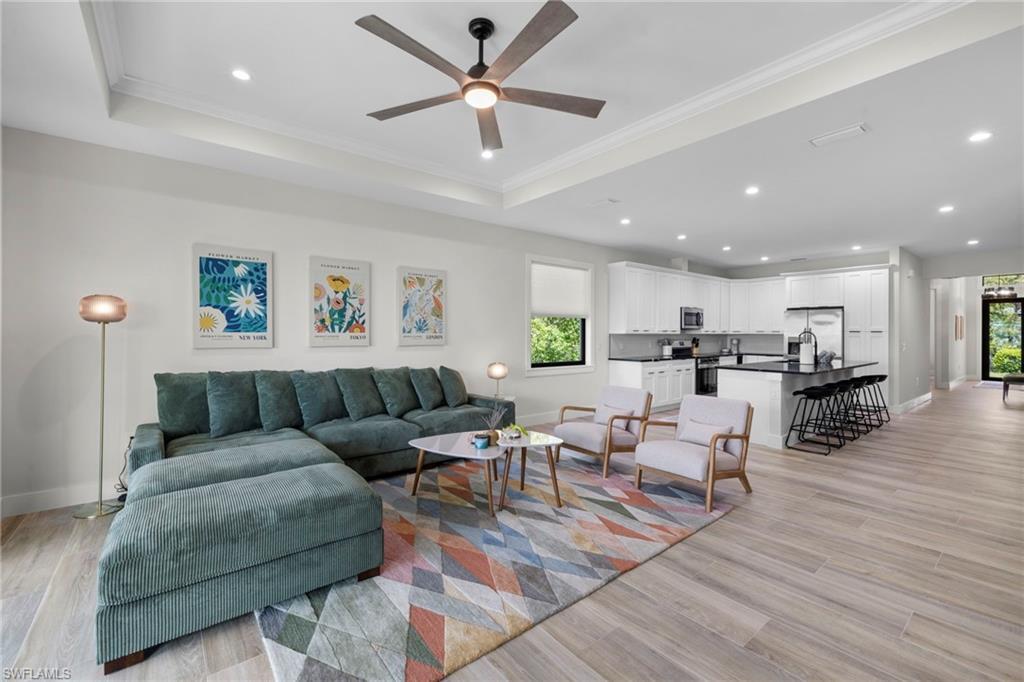 Image 4: Open-concept interior featuring wood-finish flooring, a tray ceiling with a ceiling fan, recessed lighting, white cabinetry, and a dark kitchen island with seating