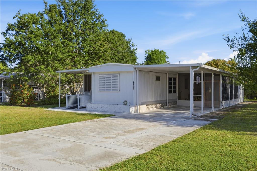 Image 4: Single-story residence featuring a white vertical siding exterior, a covered carport, and an extended screened porch