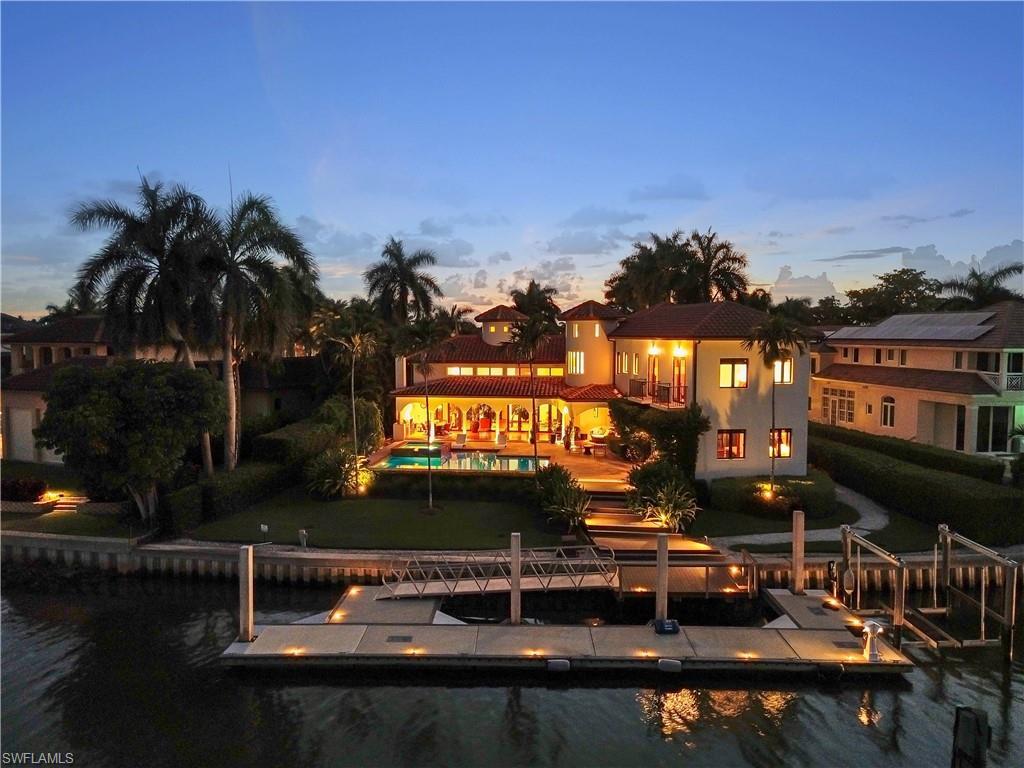 Image 4: Mediterranean-style residence featuring a terracotta tile roof, private swimming pool, waterfront access with a substantial dock, integrated boat lifts, and mature palm landscaping