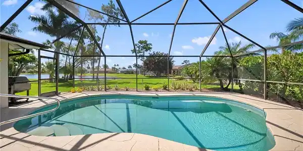 Image 3: Screened lanai featuring a freeform pool with steps, a surrounding patio with textured light-colored pavers, and mature tropical landscaping