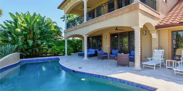Image 2: Luxurious resort-style backyard oasis featuring a sparkling saltwater pool with integrated spa, travertine decking, and a two-story Mediterranean-inspired residence with covered loggia, ceiling fans, and French doors opening to the outdoor entertaining space