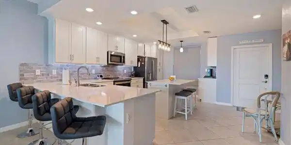 Image 4: Kitchen featuring a kitchen breakfast bar, a kitchen island, backsplash, white cabinetry, a tray ceiling and a coffee bar.