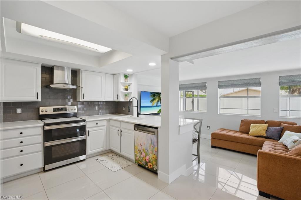 Image 4: Kitchen with appliances with stainless steel finishes, open floor plan, wall chimney exhaust hood, white cabinetry, and recessed lighting