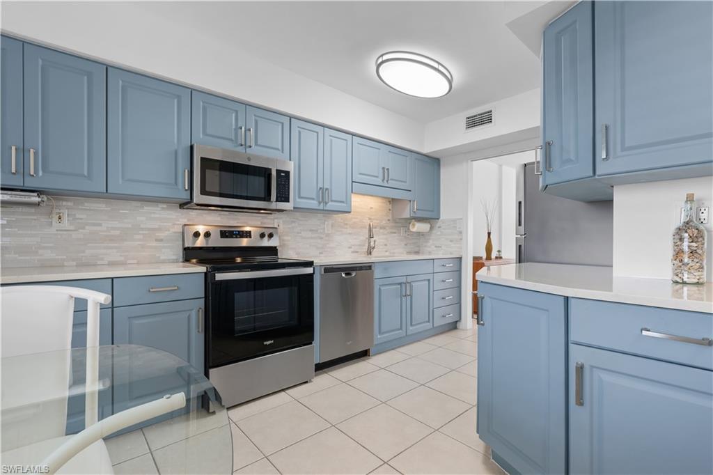 Image 4: Kitchen featuring blue cabinets, appliances with stainless steel finishes, light tile patterned floors, and decorative backsplash