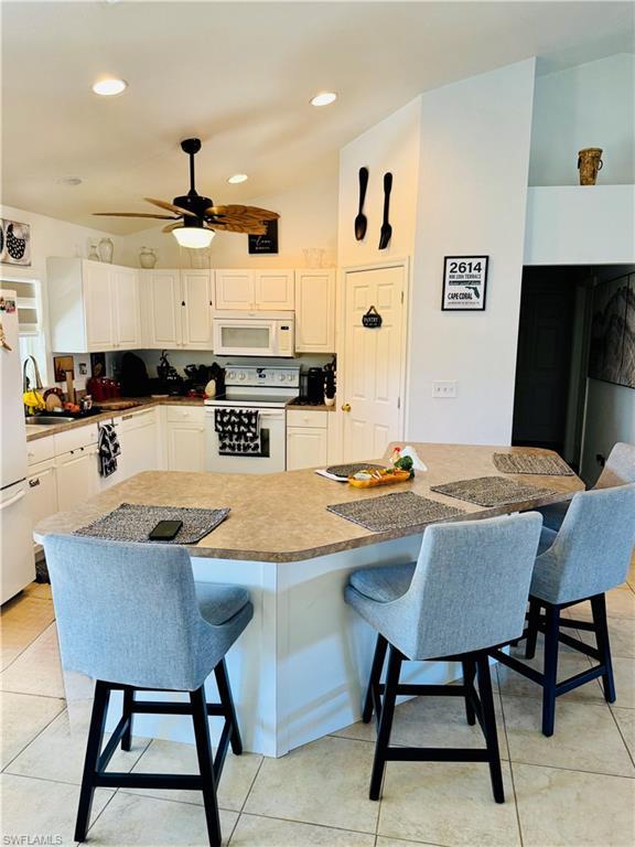 Image 4: Kitchen featuring a kitchen bar, white appliances, lofted ceiling, white cabinetry, and a center island