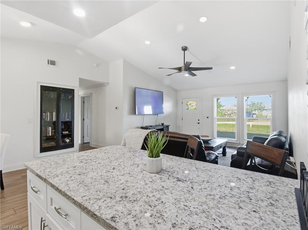 Image 2: Kitchen with light stone counters, white cabinets, ceiling fan, lofted ceiling, and open floor plan