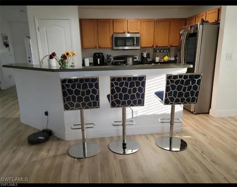 Image 4: Kitchen featuring dark countertops, stainless steel appliances, a breakfast bar area, and light wood-style floors