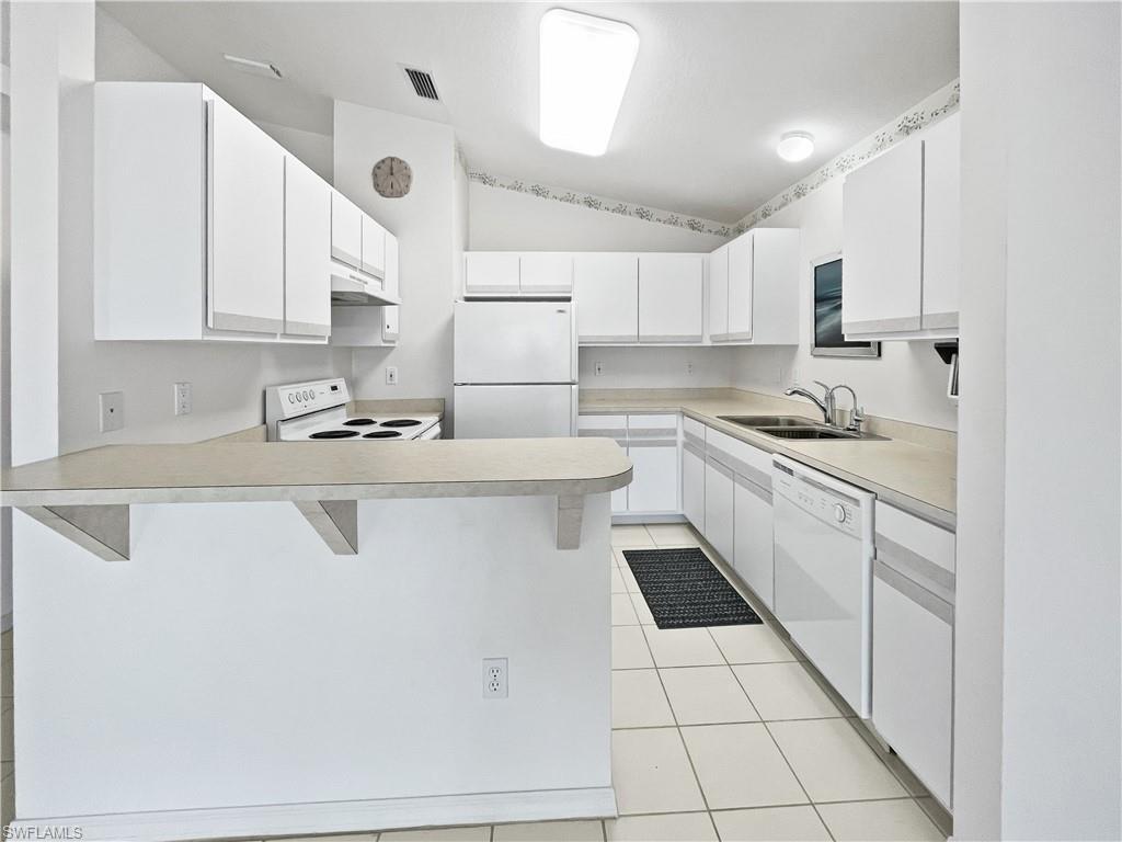 Image 4: Kitchen featuring a kitchen bar, white cabinets, white appliances, lofted ceiling, and light countertops