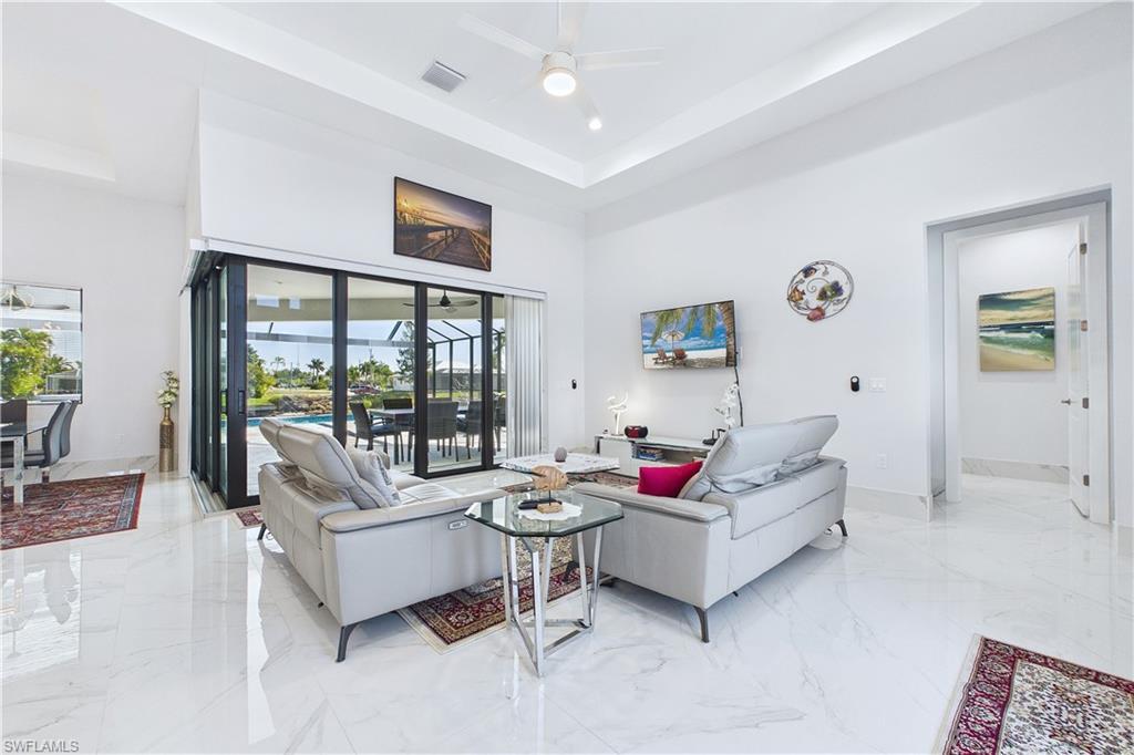 Image 4: Living room with light marble finish floors, a high tray ceiling, and ceiling fan