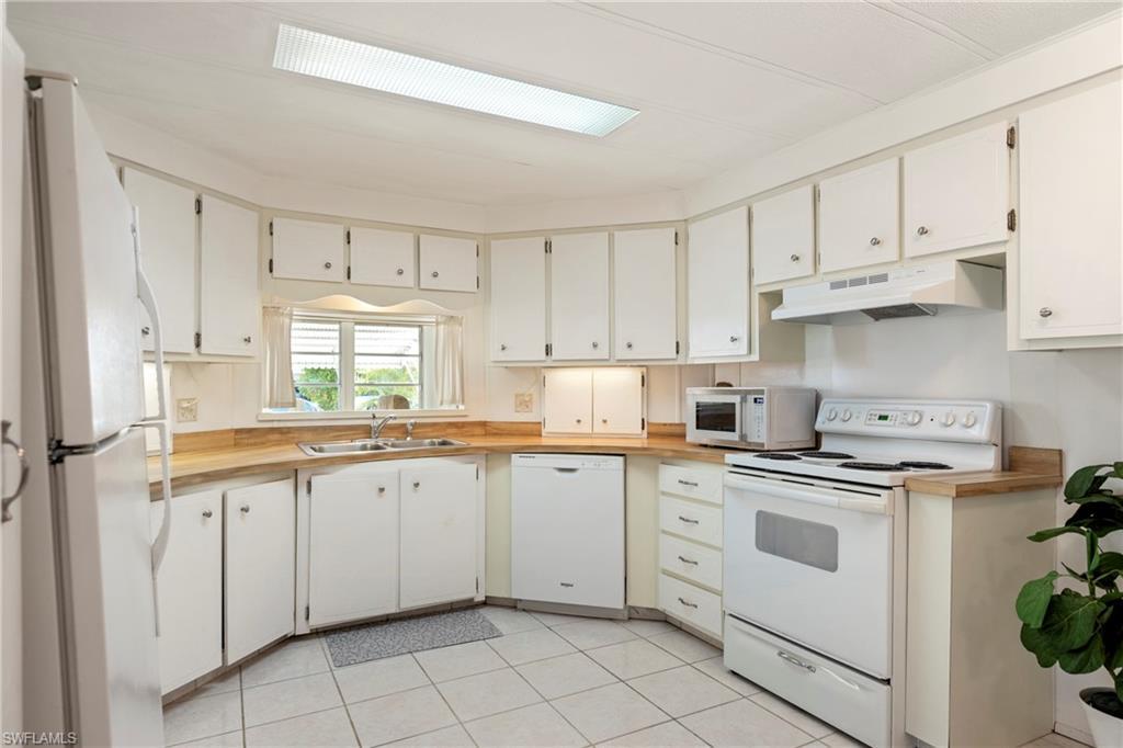 Image 3: Kitchen with white appliances, white cabinets, light tile patterned floors, and wooden counters