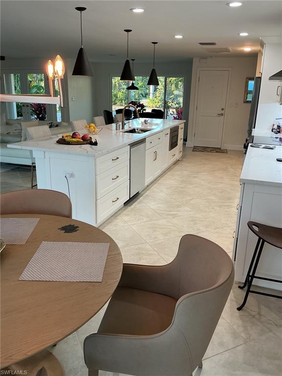 Image 3: Kitchen with white cabinets, light stone counters, a breakfast bar area, a large island, and decorative light fixtures