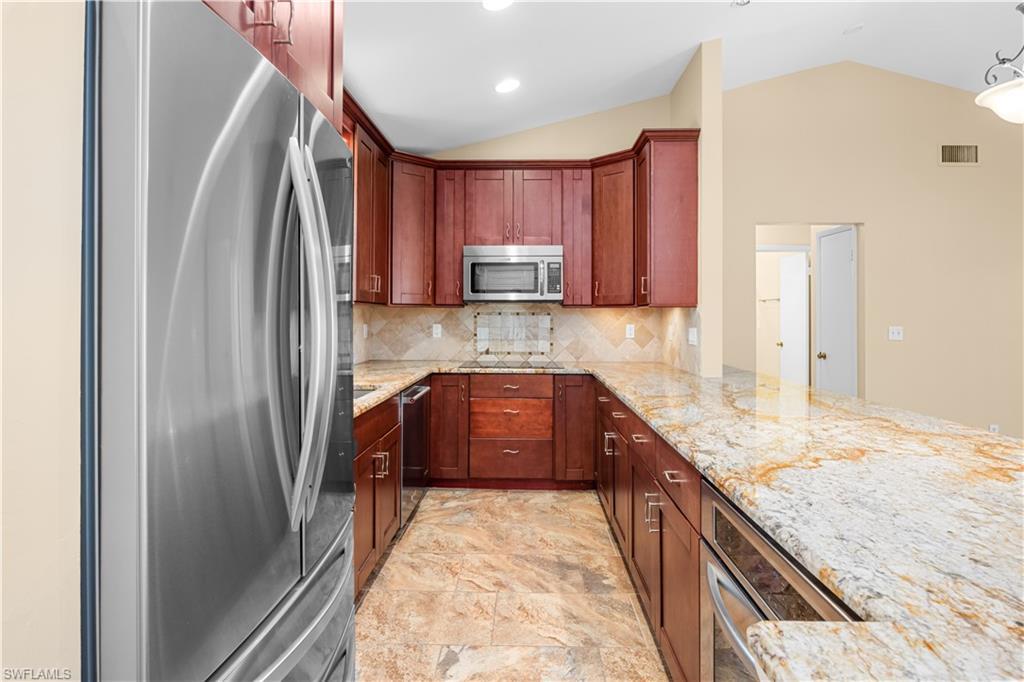 Image 3: Kitchen with stainless steel appliances, light stone countertops, lofted ceiling, decorative backsplash, and pendant lighting