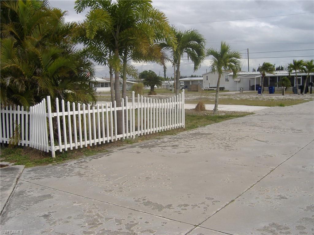 Image 2: The property features a white picket fence, mature palm trees, and a concrete driveway