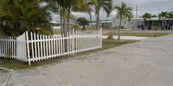 Image 2: The property features a white picket fence, mature palm trees, and a concrete driveway