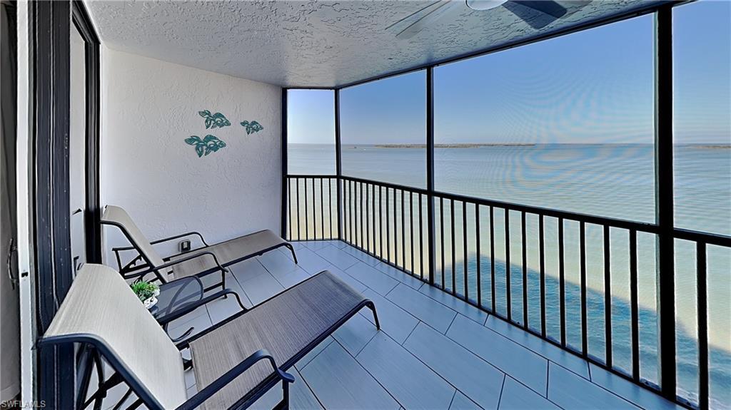 Image 2: Screened balcony featuring expansive water scenery, textured walls, a ceiling fan, and light-toned tile flooring