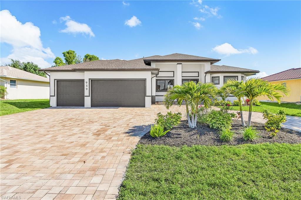 Image 1: Contemporary single-story residence featuring a paved driveway, two-car garage, manicured lawn, and tropical landscaping