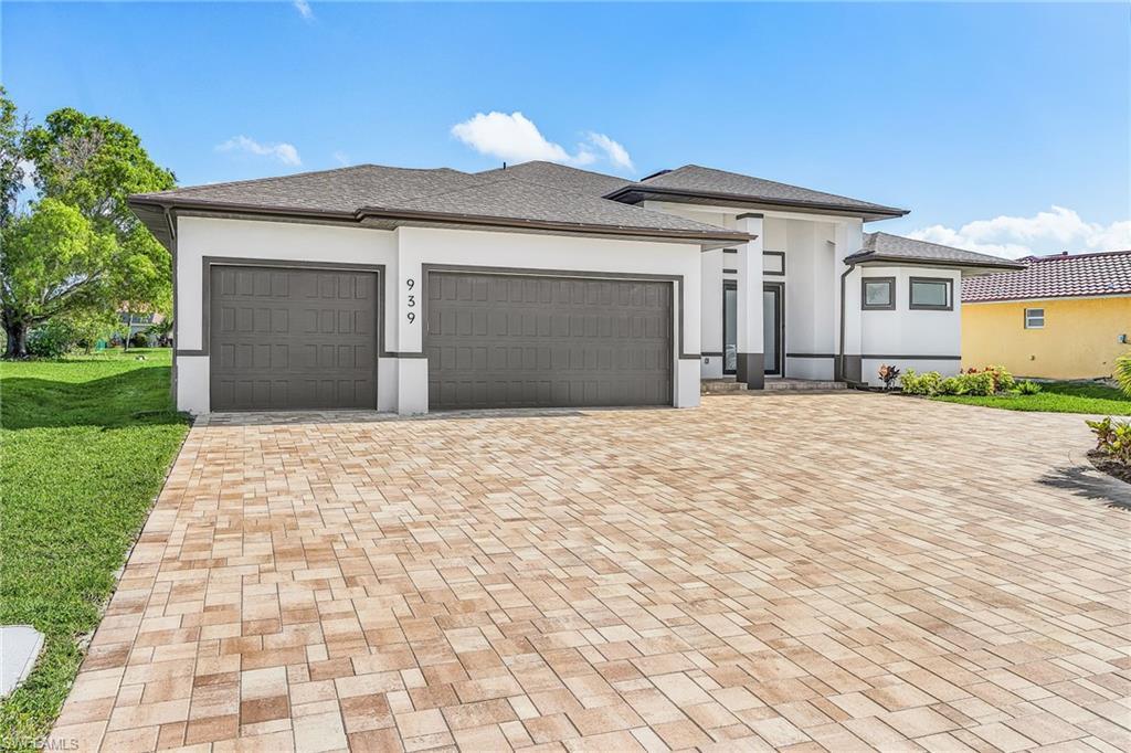 Image 2: Contemporary exterior featuring a paver driveway, two-car garage, white stucco facade with dark trim, and a covered entry