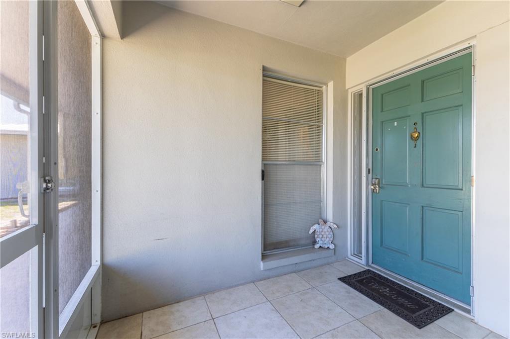 Image 4: Entryway featuring a paneled turquoise door with brass hardware, sidelite, screened enclosure, and tiled flooring