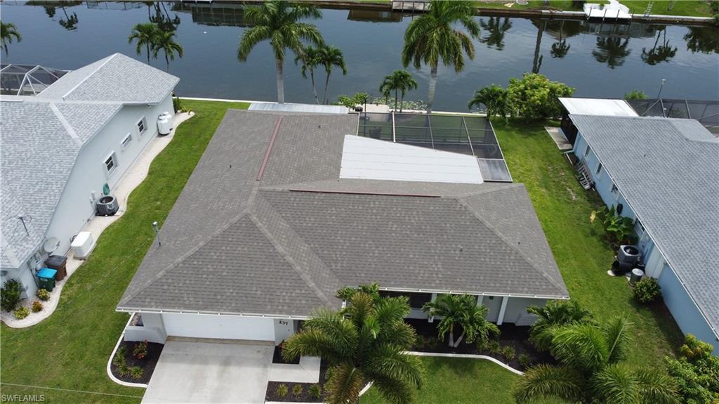 Image 2: Waterfront property featuring a private boat dock, screened pool enclosure, mature palm trees, and an attached garage with concrete driveway