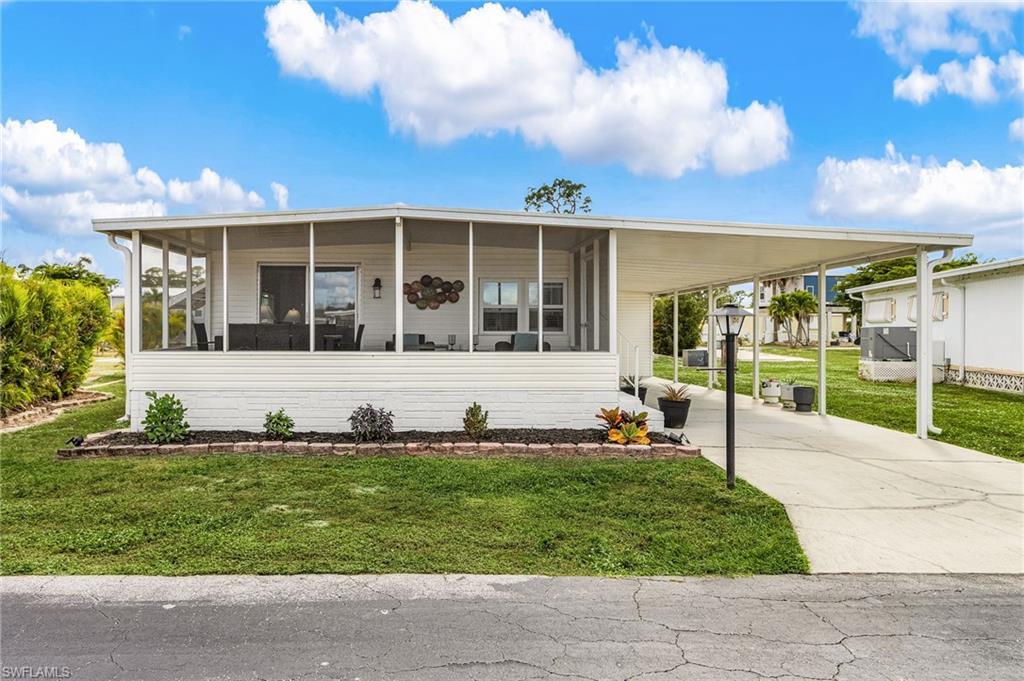 Image 2: White siding residence featuring a screened-in porch, covered carport, concrete driveway, and a front garden bed with dark mulch