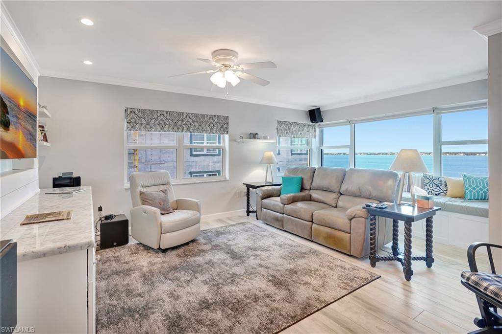 Image 3: Living room with river view, crown molding, wood-like tile floor, impact windows.