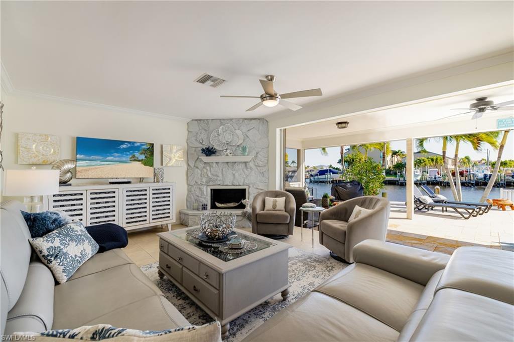 Image 3: Living area with tile patterned flooring, a ceiling fan, a stone fireplace, and ornamental molding