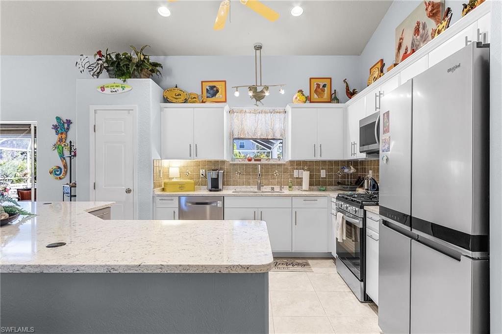 Image 4: Kitchen with stainless steel appliances, white cabinets, tasteful backsplash, light tile patterned flooring, and hanging light fixtures