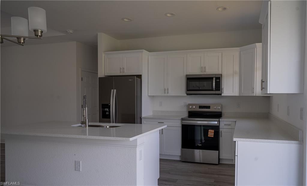 Image 4: Bright kitchen featuring white cabinetry, light-toned countertops, stainless steel appliances, a kitchen island with an undermount sink, and wood-finish flooring