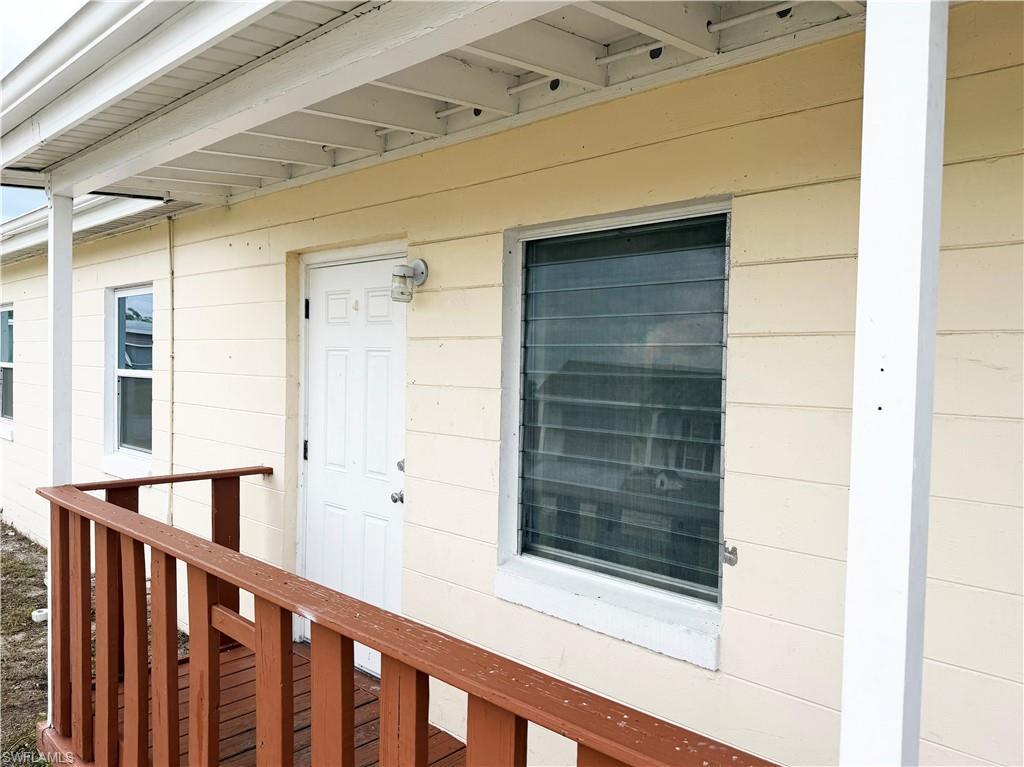 Image 2: Cream-colored horizontal siding exterior featuring a white paneled entry door, an exterior wall light fixture, and a brown wood-finish porch railing