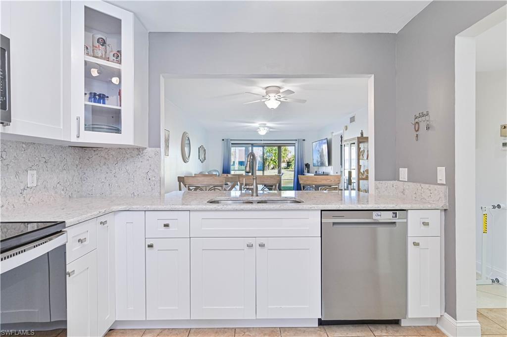 Image 3: Kitchen with white cabinets, light stone counters, stainless steel appliances, and glass insert cabinets
