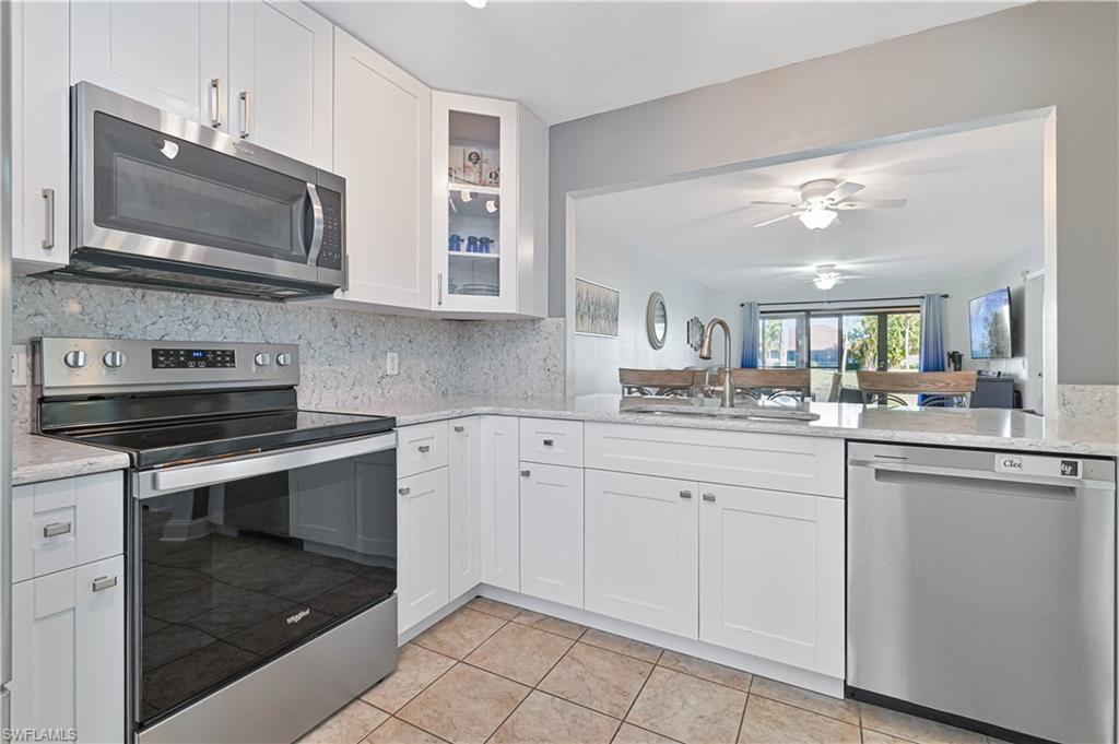 Image 4: Kitchen with appliances with stainless steel finishes, glass insert cabinets, light stone countertops, and white cabinetry